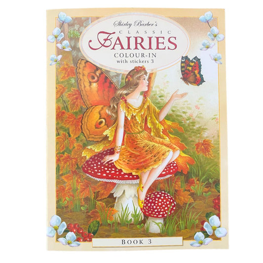 cover of Shirley Barber classic Fairies colour in book with stickers book . Shows a fairy in orange tones sitting on a red spotted mushroom and reaching out to a butterfly